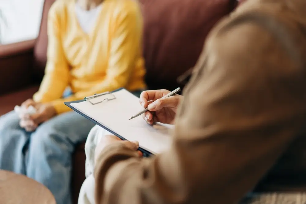 Psychologue prenant des notes sur un dossier lors d'un entretien de recrutement avec un candidat.
