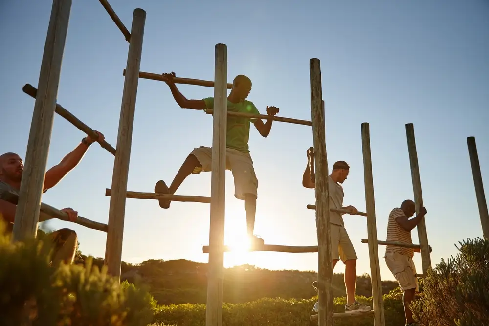 Des hommes franchissent une structure en bois lors d'un entraînement sur un parcours d'obstacles en plein air.