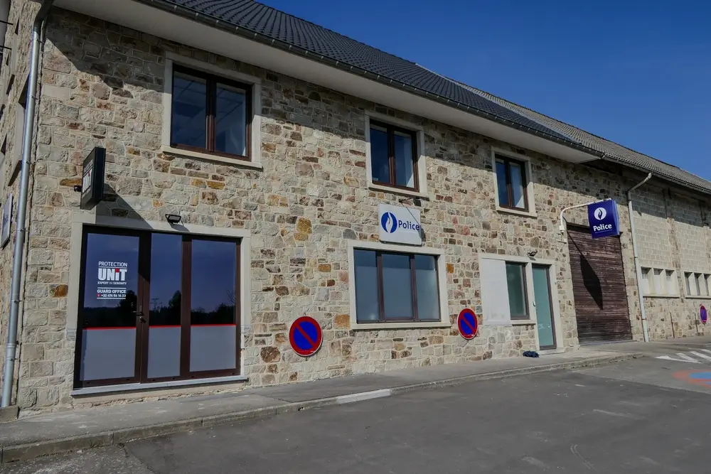 Commissariat de police belge à façade en pierre avec enseignes officielles et panneaux de signalisation.