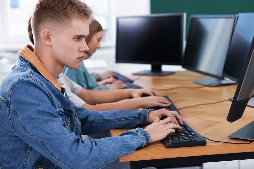 Un candidat passe un test sur ordinateur dans une salle d'examen informatique avec d'autres participants.
