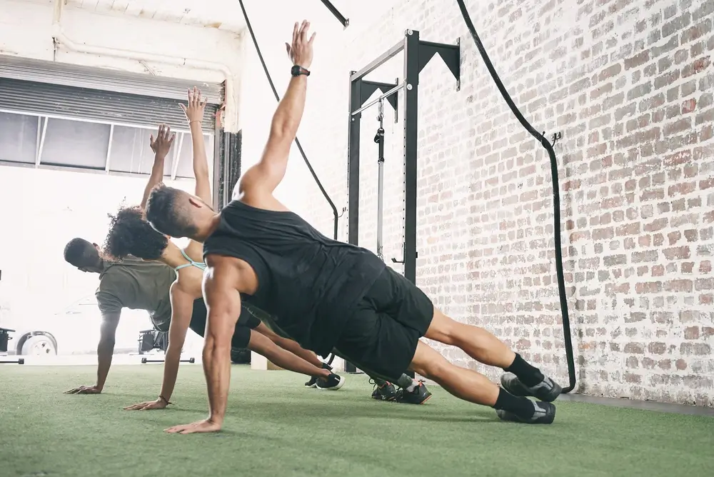 Trois sportifs font du gainage latéral pour leur entraînement de fitness training workout et leur préparation physique.