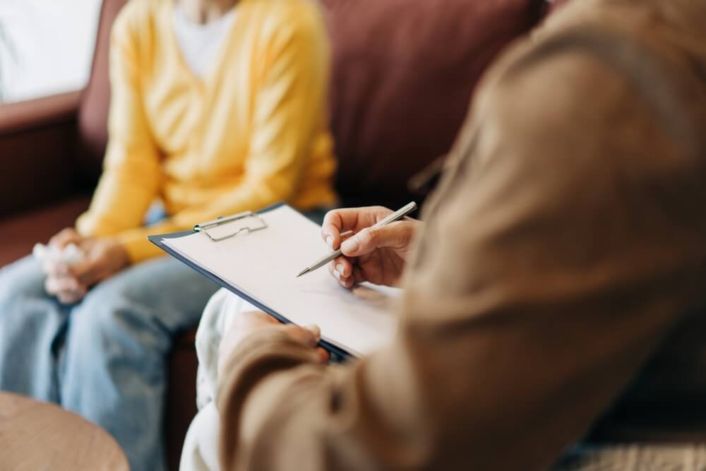 Selectiepsycholoog die aantekeningen maakt in een dossier tijdens een selectiegesprek met een kandidaat-politieagent.