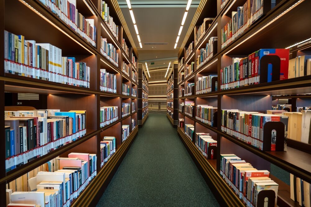Verlicht gangpad in een bibliotheek vol boeken, een ideale omgeving voor studie en voorbereiding op de selectieproeven van de politie.