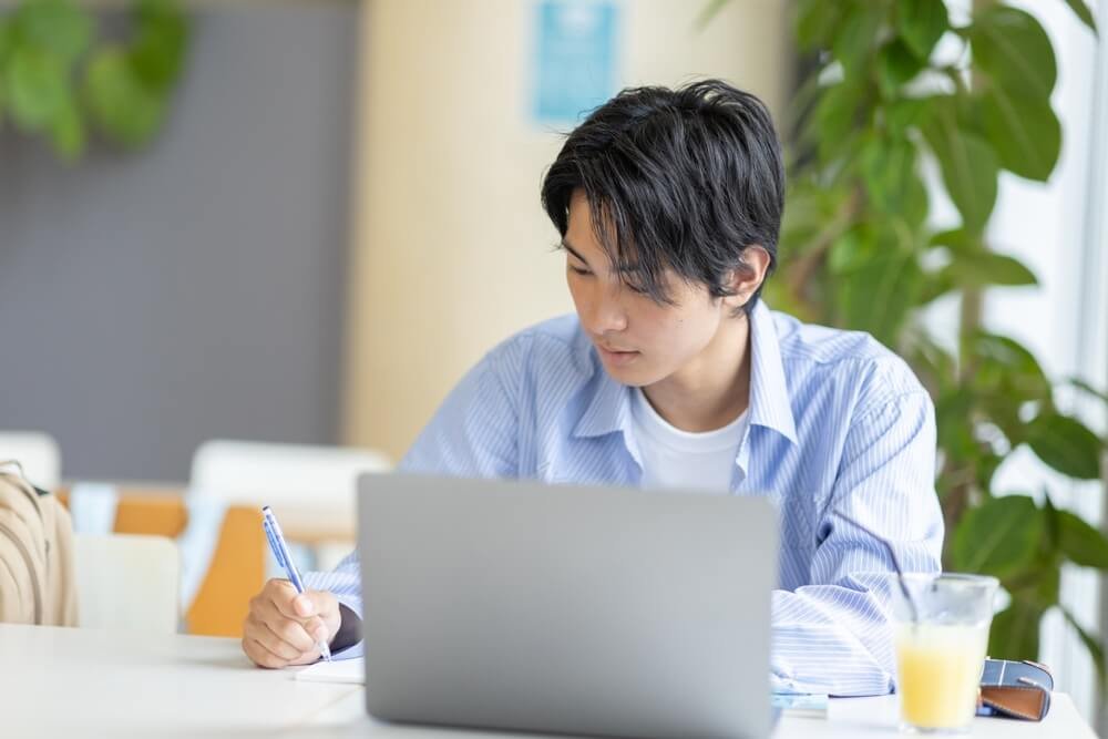Geconcentreerde student voor een laptop, die notities maakt ter voorbereiding op de selectieproeven van Jobpol.