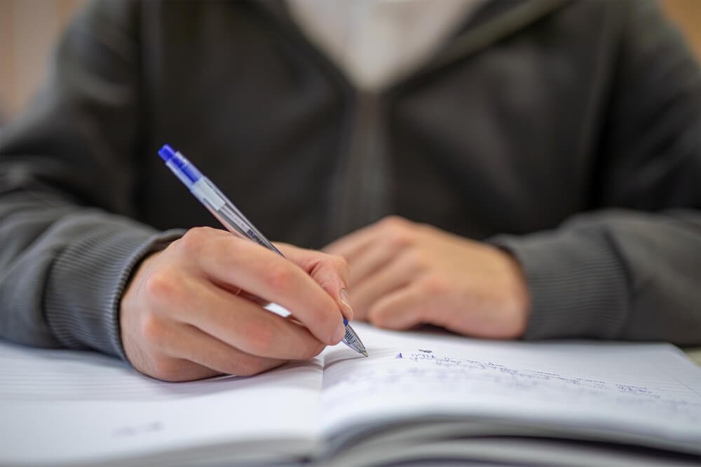 Hand van een persoon die in een schrift schrijft om fouten te analyseren en zich voor te bereiden op een examen.