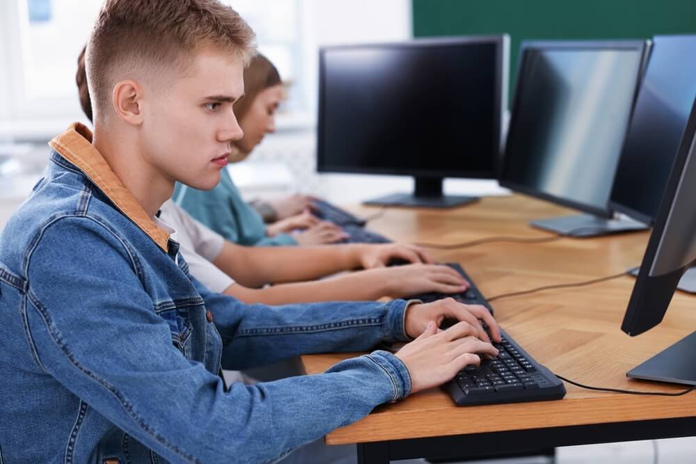 Een kandidaat legt een computertest af in een examenlokaal voor informatica samen met andere deelnemers aan de politieselectie.