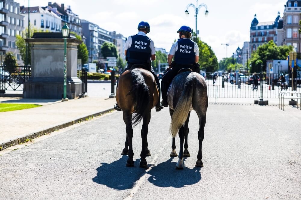 Twee Belgische ruiters van de politie te paard op patrouille in de straat, in uniform met het opschrift Politie Police.