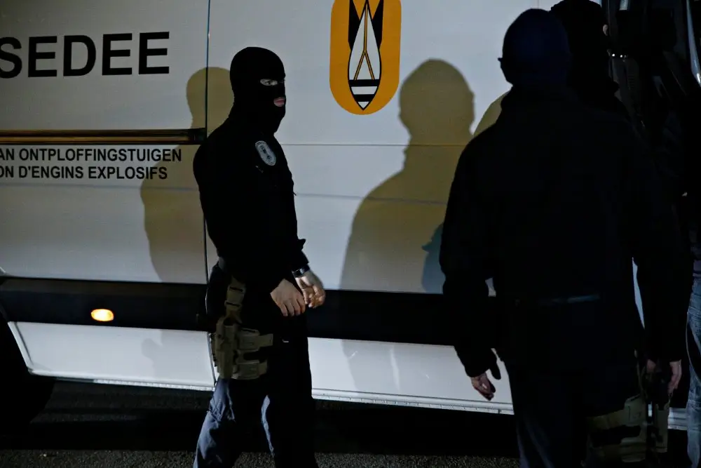 Membres des forces spéciales en équipement tactique noir et cagoules devant un véhicule de déminage du SEDEE.