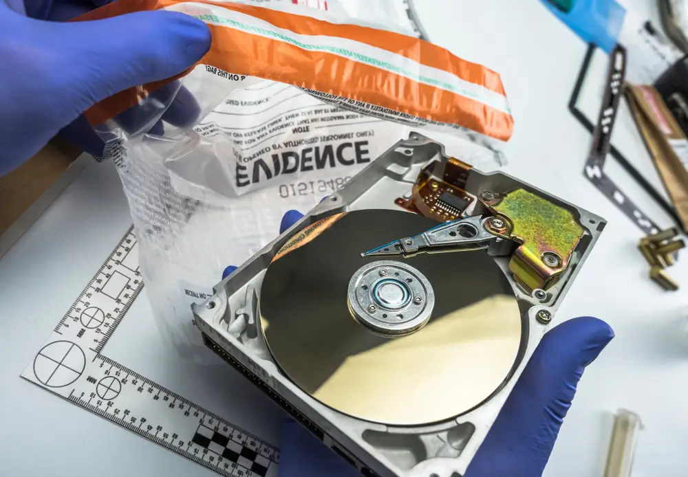 Digitaal forensisch onderzoeker met blauwe handschoenen inspecteert een geopende harde schijf en bewijszak.