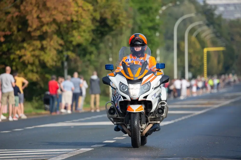 Belgische politiemotorrijder in beschermende kledij op zijn motor tijdens een officiële escorte-opdracht.