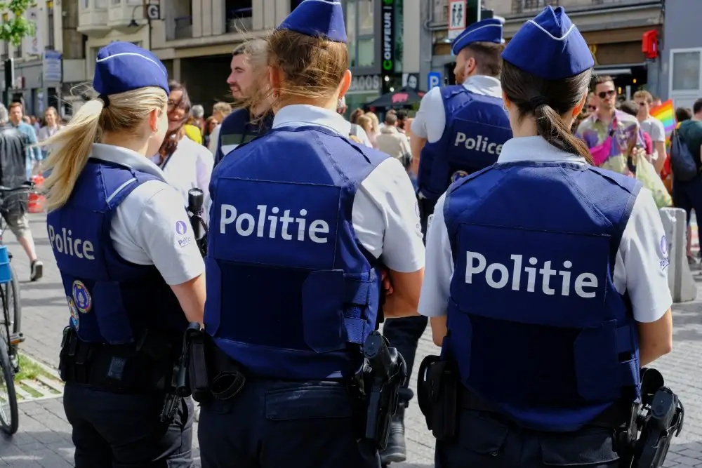 Policiers en patrouille vus de dos, portant l'uniforme bleu avec marquage Politie et Police dans une rue animée.