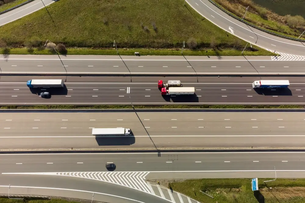 Luchtfoto van een Belgische autosnelweg met vrachtwagens en auto's, ter illustratie van verkeersdoorstroming en infrastructuur.