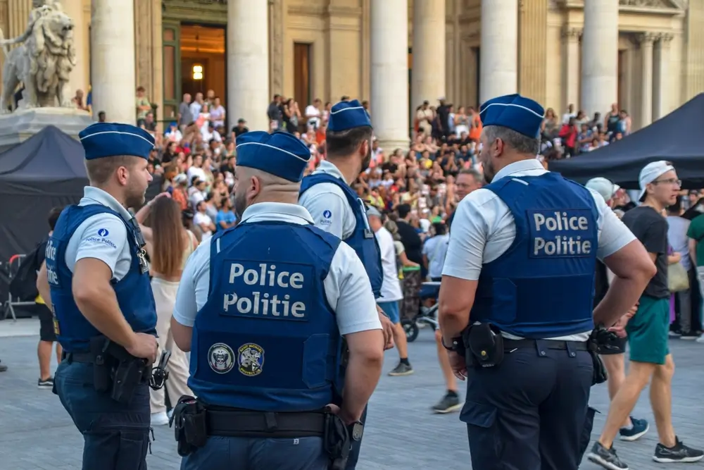 Policiers belges en patrouille urbaine se concertant lors d'une opération de maintien de l'ordre devant une foule.