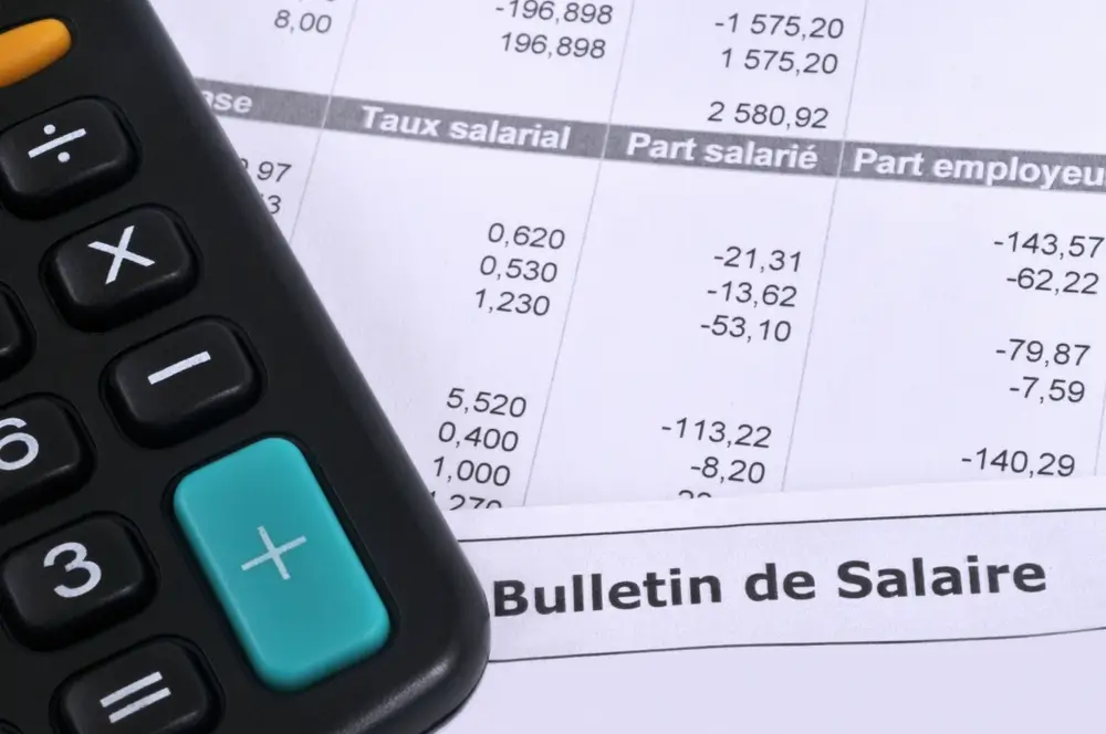 Mains tenant une fiche de salaire avec des billets et une calculatrice sur un bureau