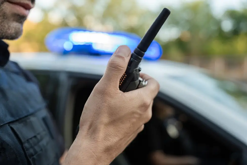 Politieagent met een radio voor een interventievoertuig met blauwe zwaailichten tijdens een opleidingsoefening.