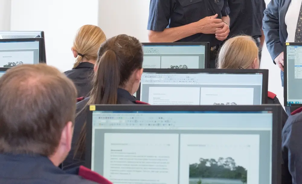 Politieagenten in opleiding voor beeldschermen, ter illustratie van de werkomgeving en sociale voordelen van de functie.