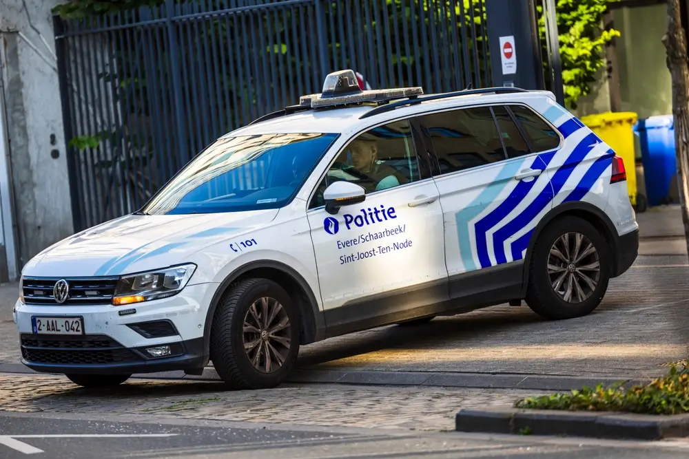 Patrouille de police de proximité dans une rue belge avec un véhicule sérigraphié, illustrant le métier d'inspecteur.
