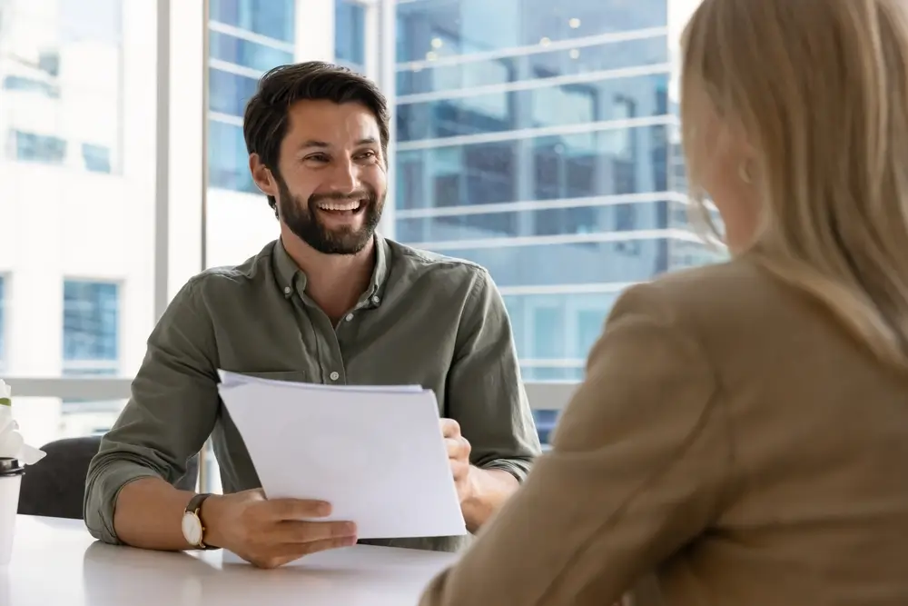 Candidat souriant tenant son CV lors d'un entretien d'embauche face à une recruteuse pour une sélection.