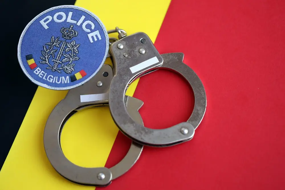 Insigne van de Belgische politie en handboeien op een driekleurige achtergrond, als symbool voor justitie en wetshandhaving.
